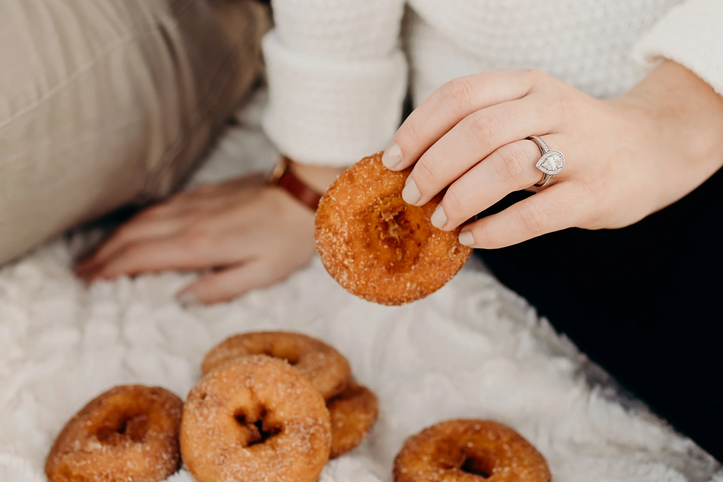 Woman picks up a donut showing off her pear shaped engagement ring.