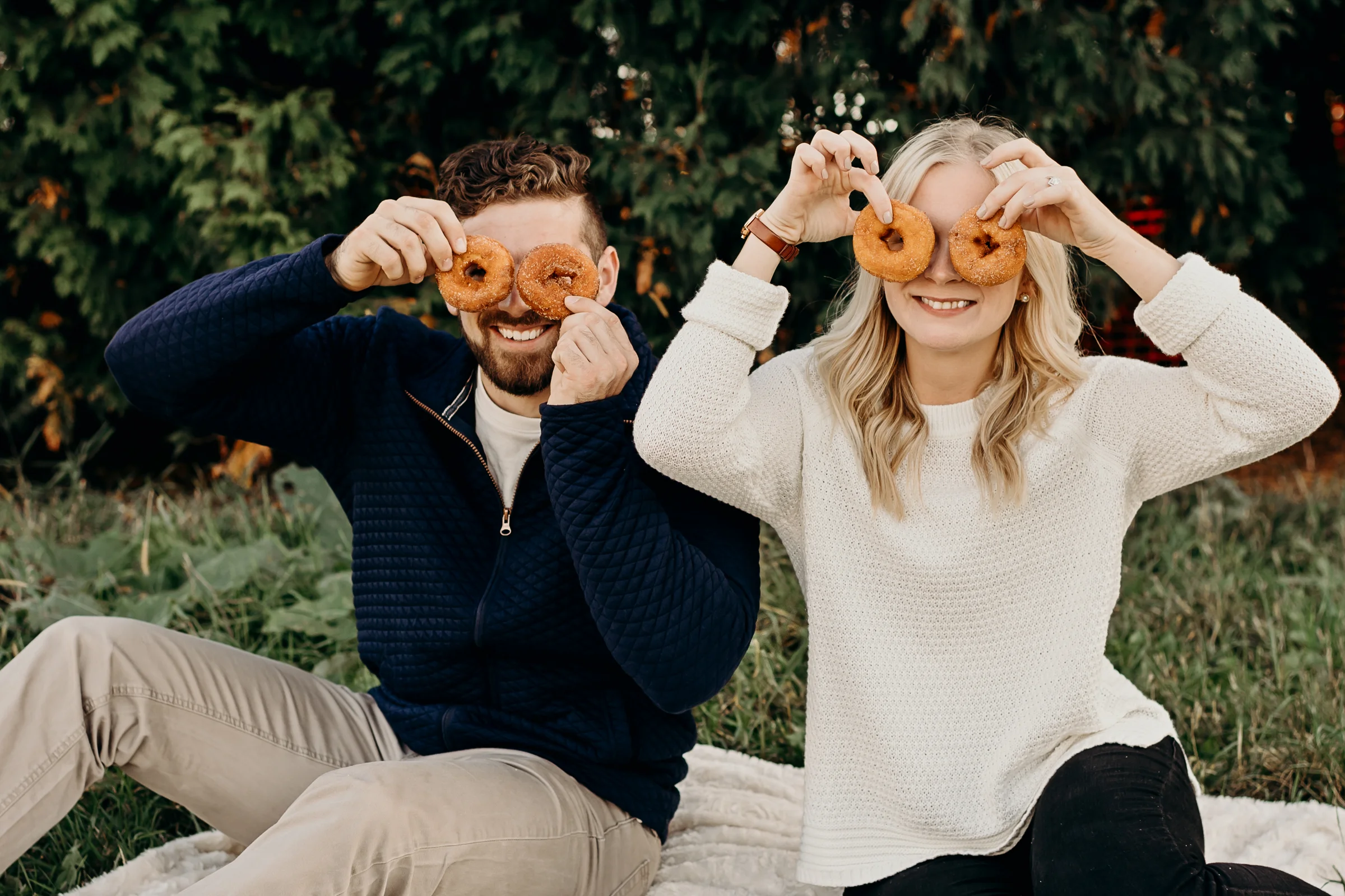 Engaged couple playfully holds donuts over their eyes.