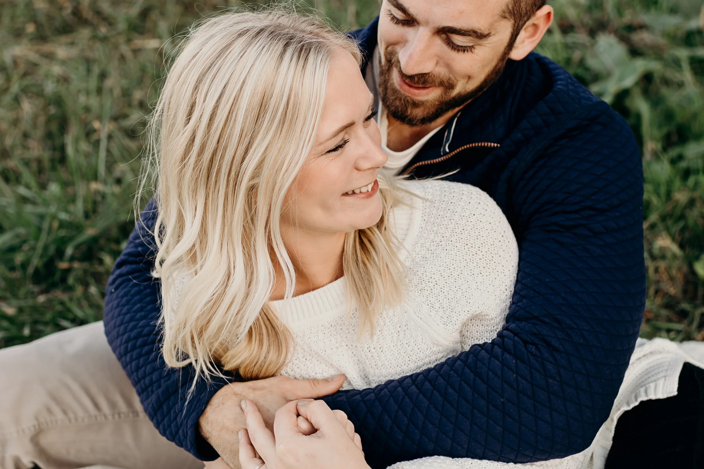 Man wraps his arms around his fiancé and makes her smile.