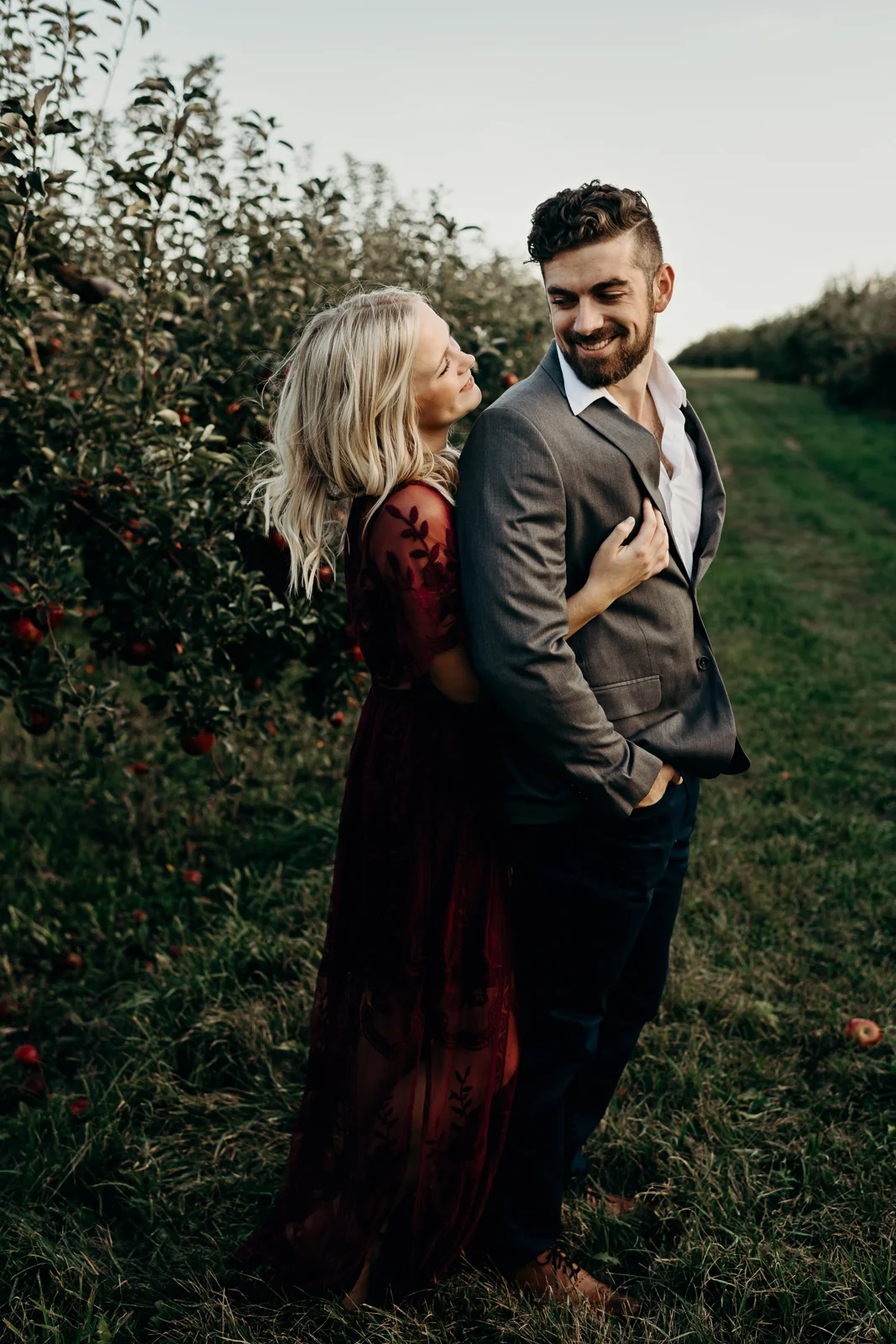Man looks back at his fiancé as she wraps her arms around him from behind.