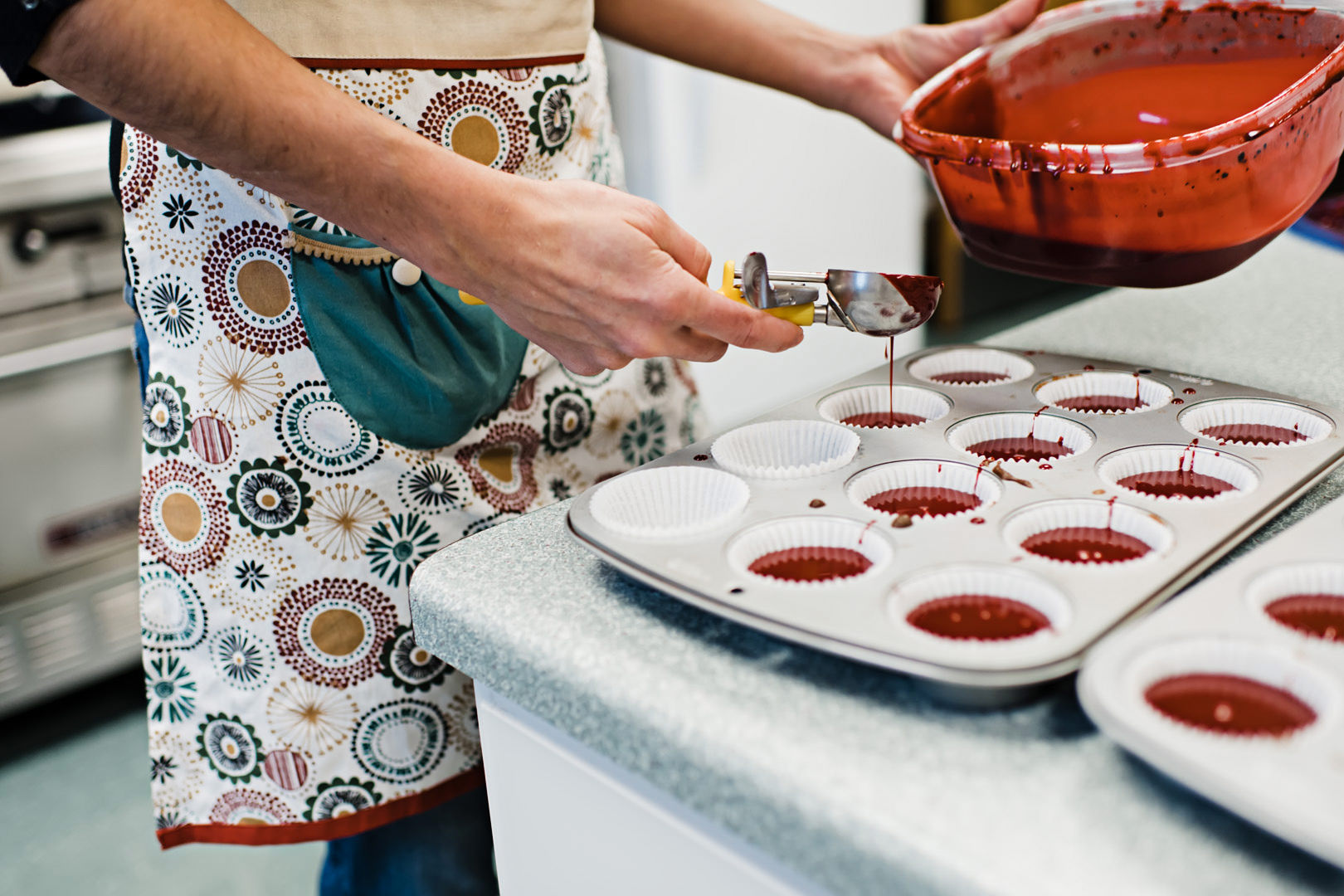 Scooping red velvet cupcake batter into muffin pan