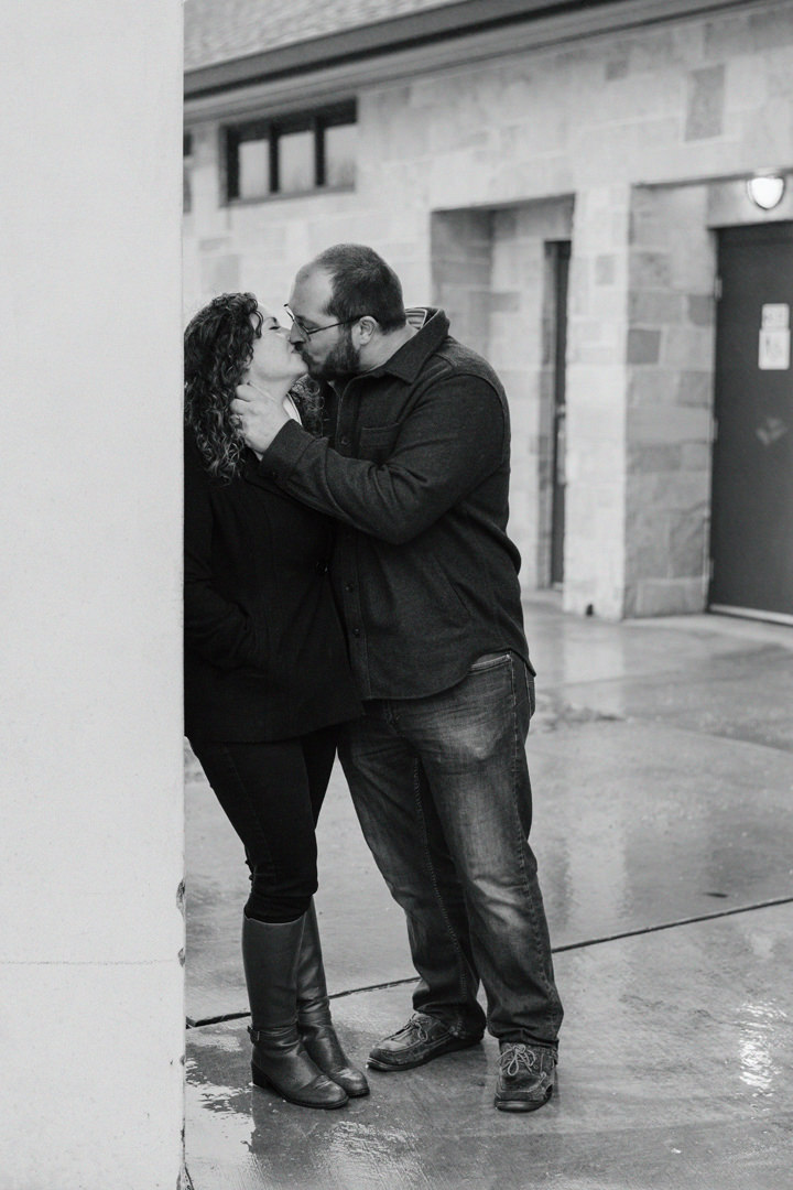 Engaged couple leaning on a pillar and kissing