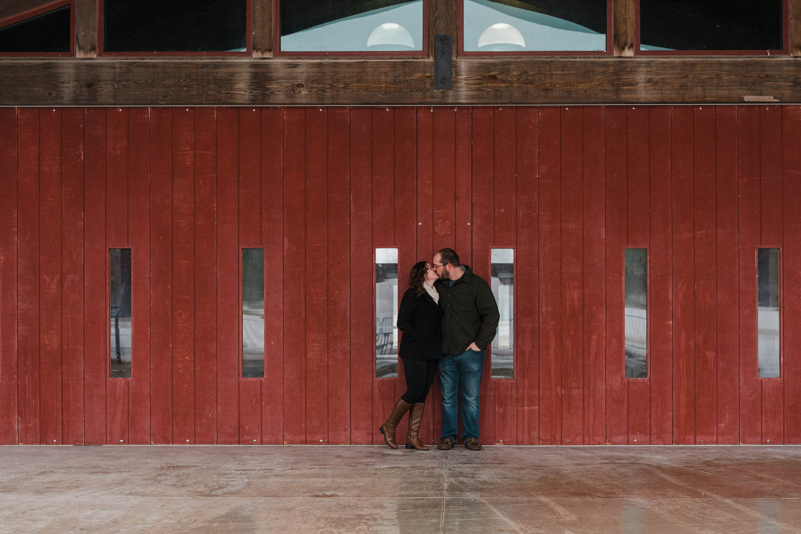 Engaged couple kissing in front of red barn wood building