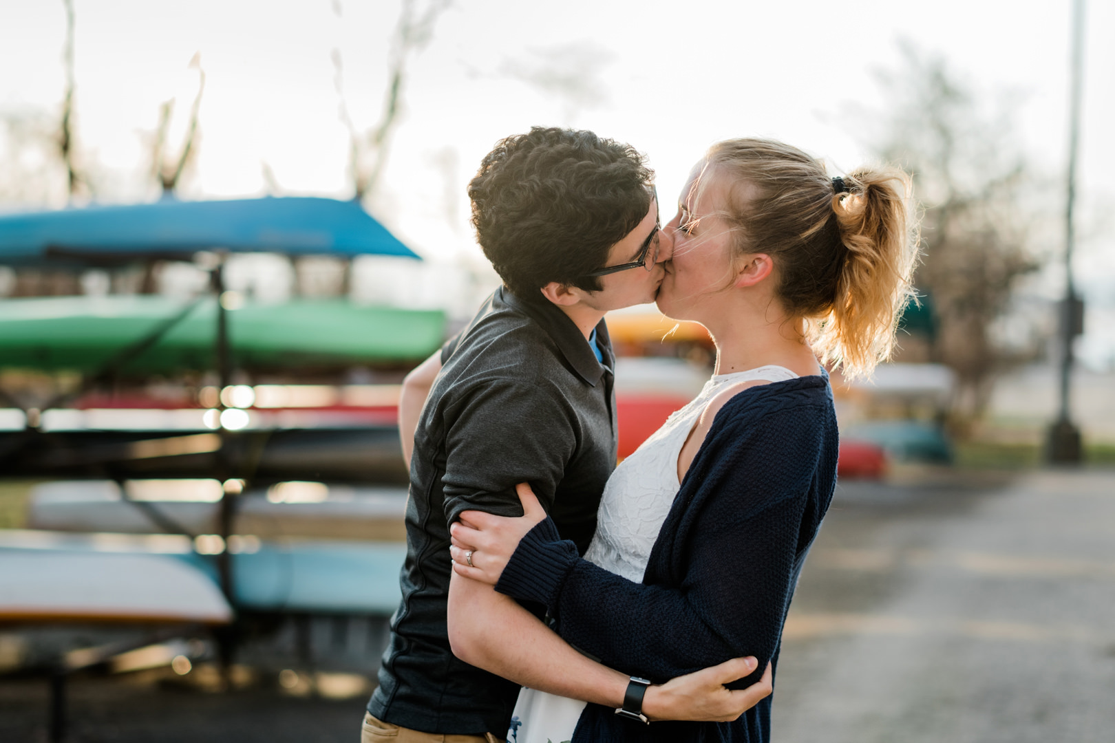 Engaged couple kissing by colorful canoes