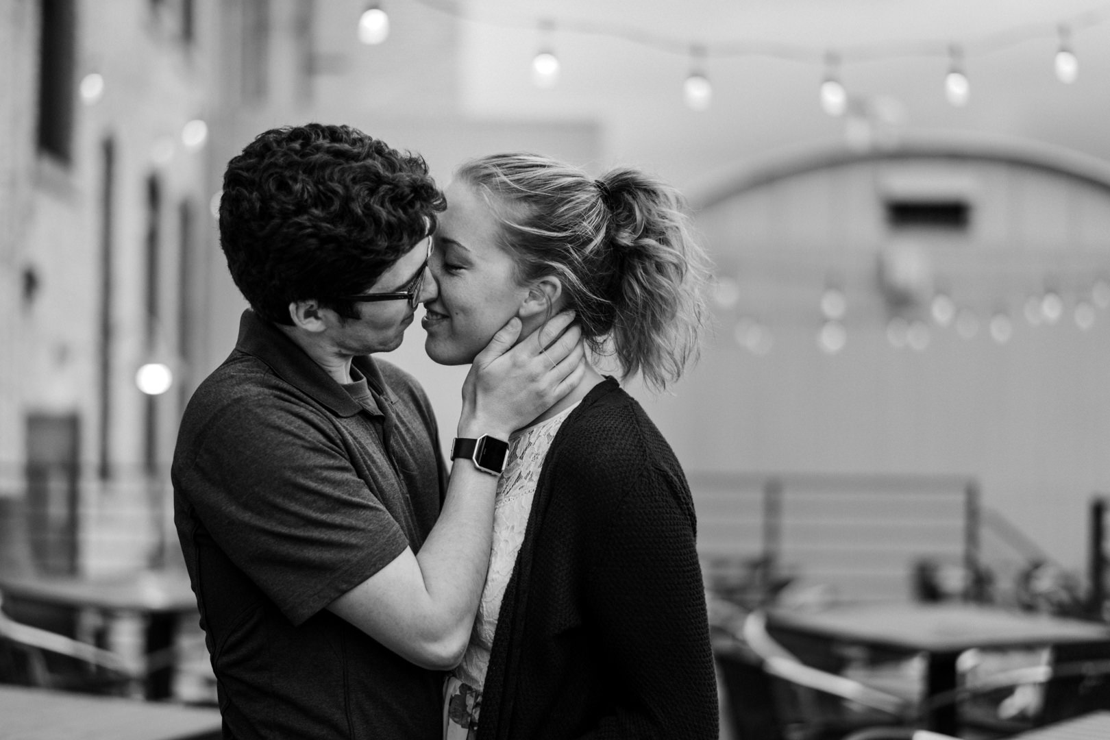 Engaged couple about to kiss by string lights