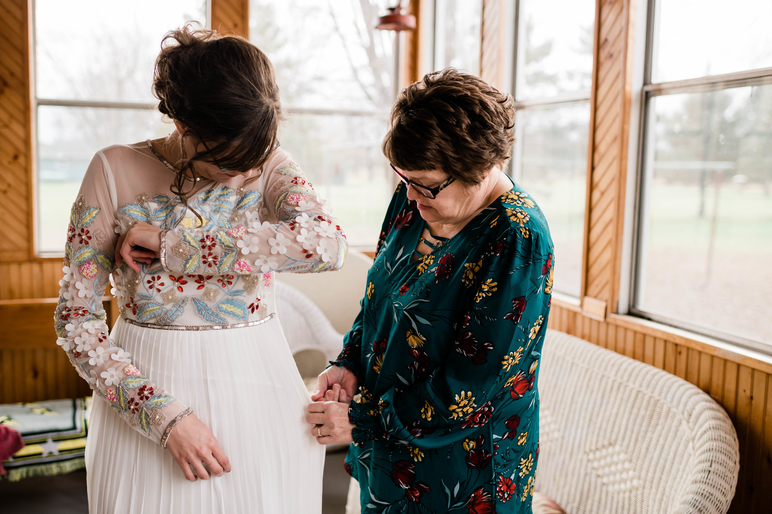 Mother helps her daughter zip up her wedding dress