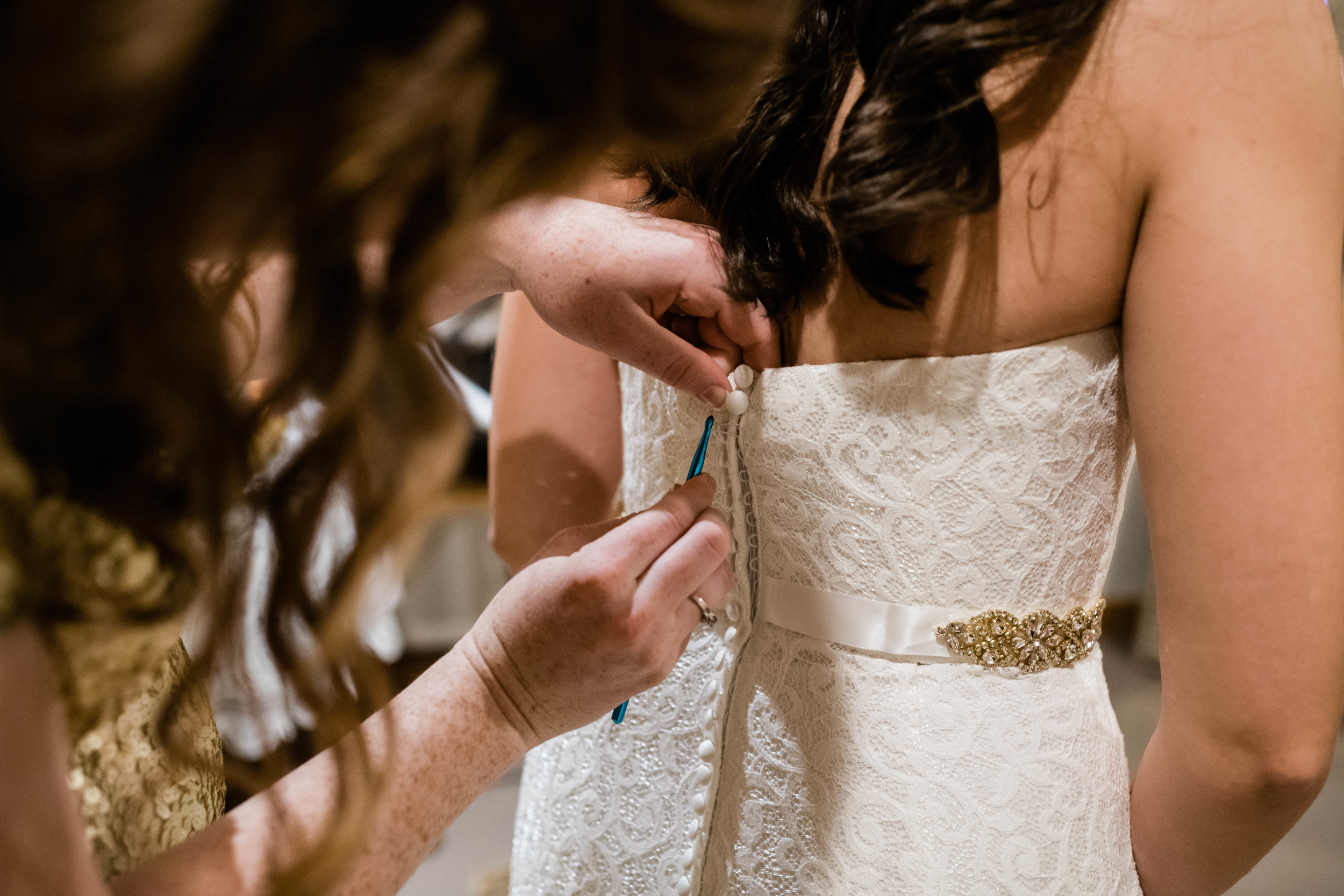 Bridesmaid using crochet hook to fasten bride's wedding dress