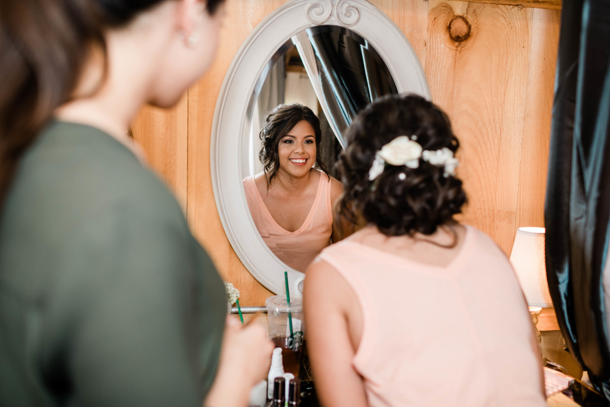 Bride looks happily in the mirror at her wedding day hair and makeup