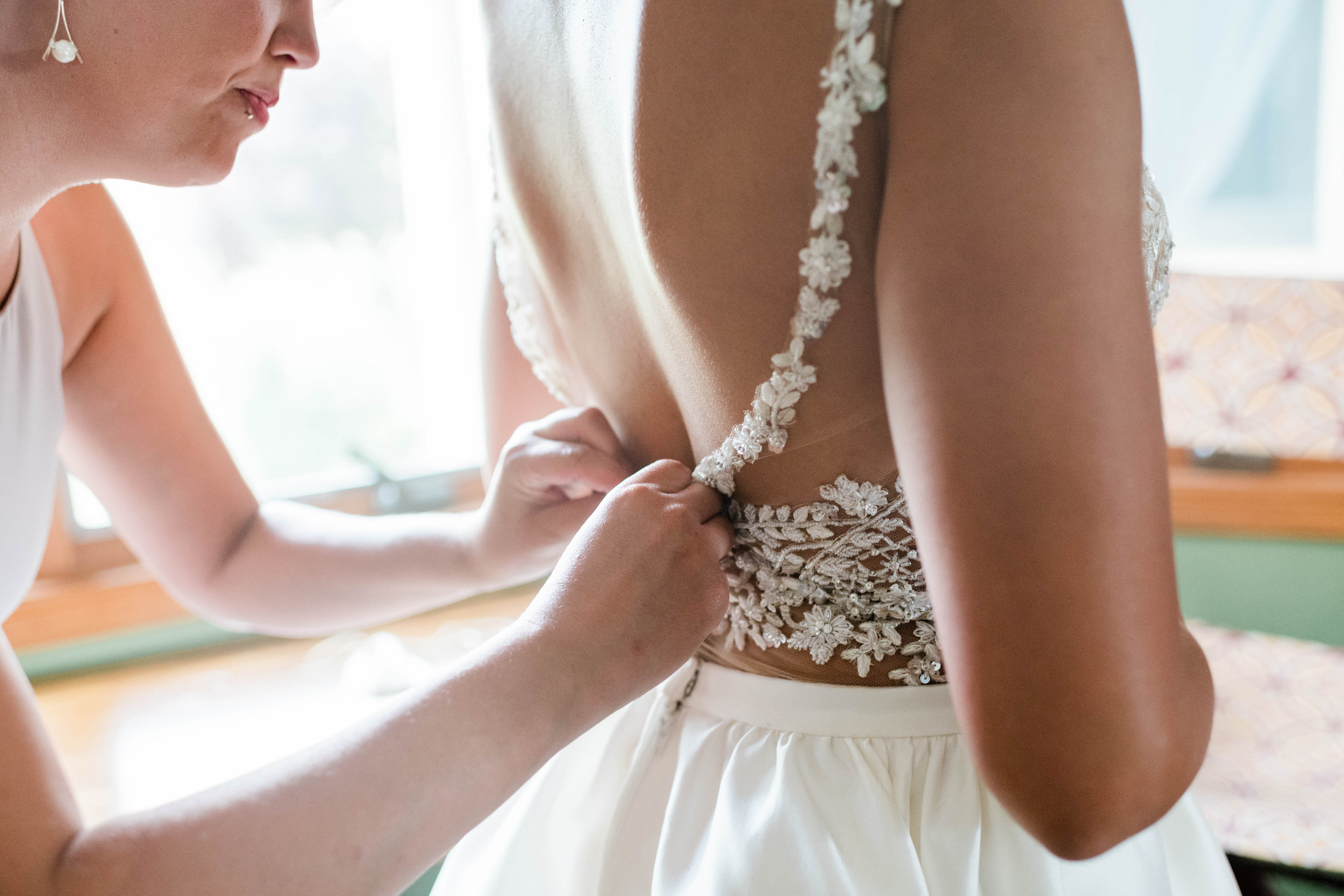 Bridesmaid buttons up bride's wedding dress