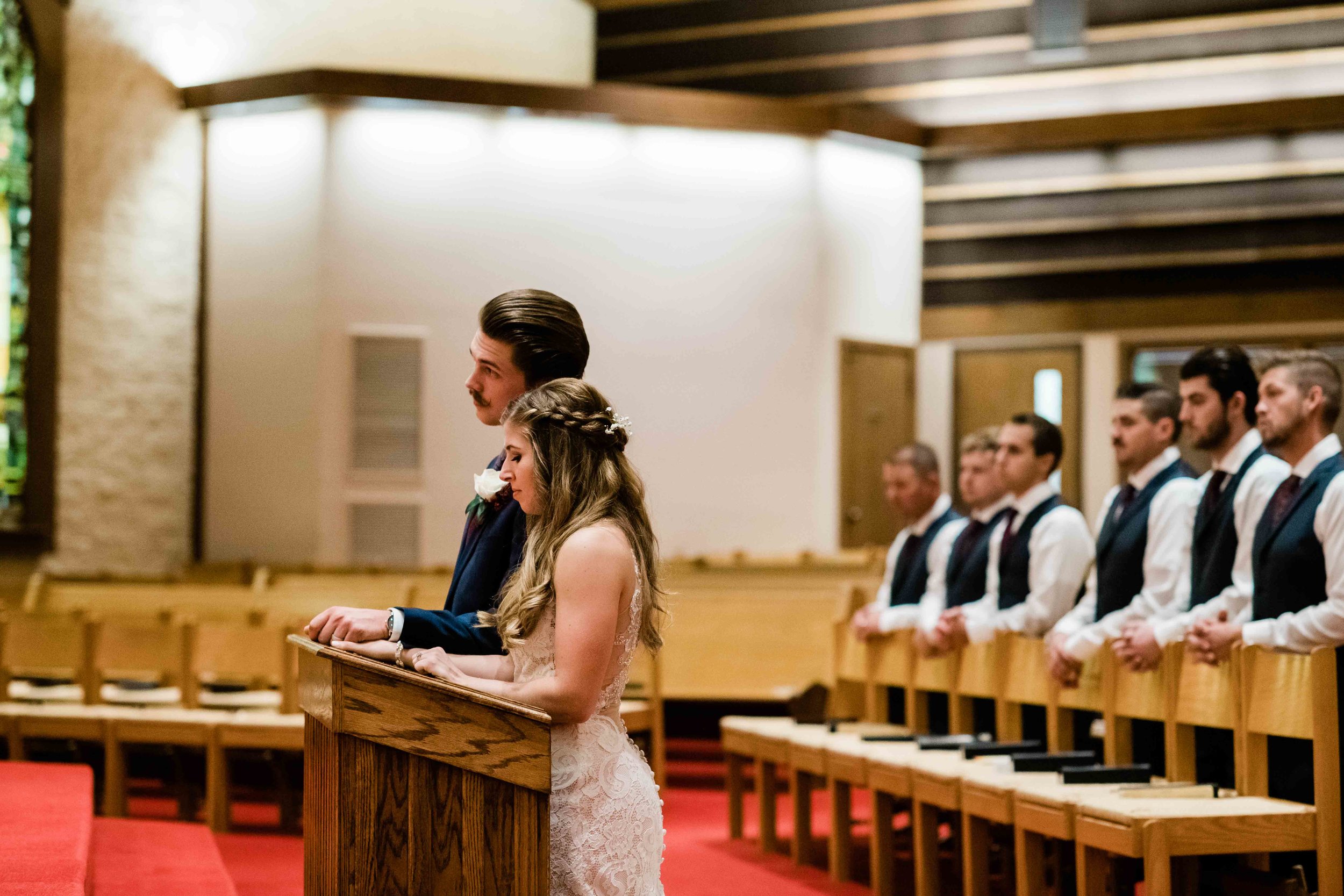 Bride and groom kneel during Catholic wedding ceremony