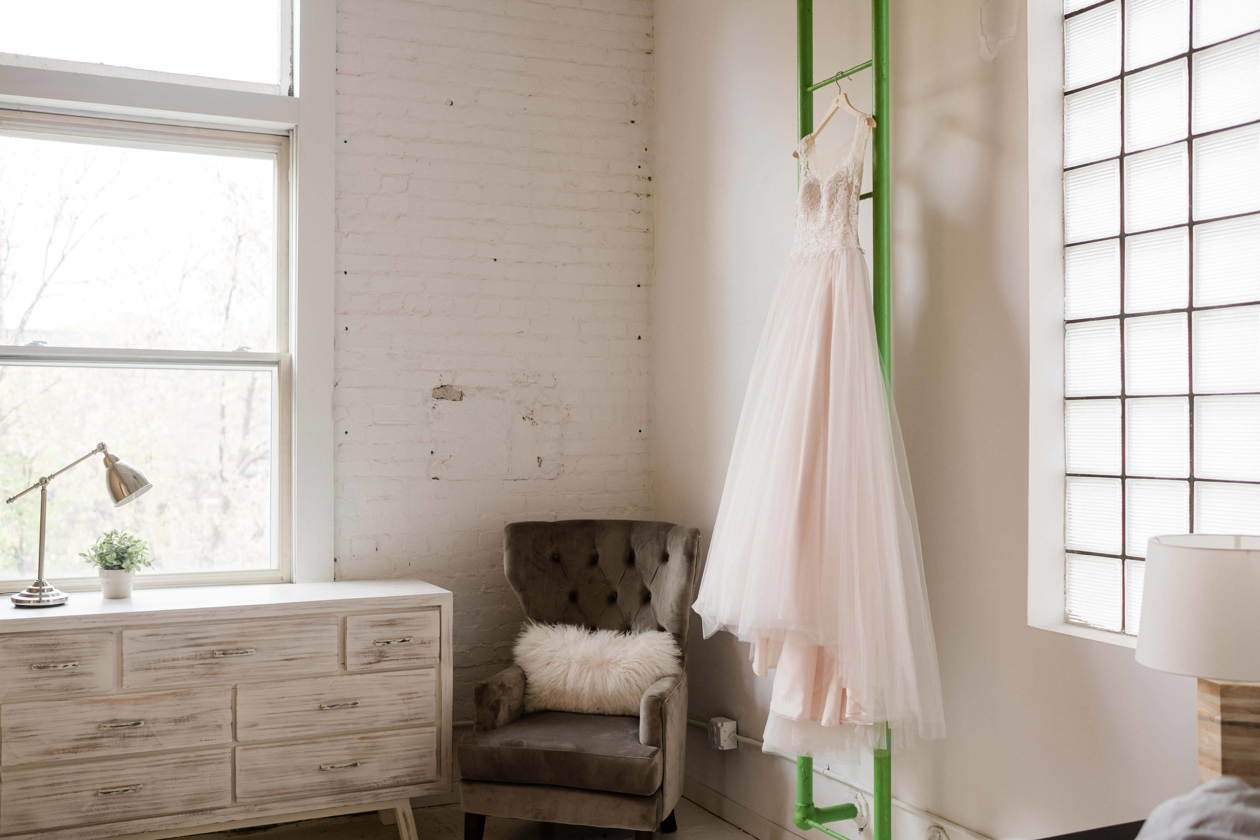 Blush pink wedding dress hanging on green ladder