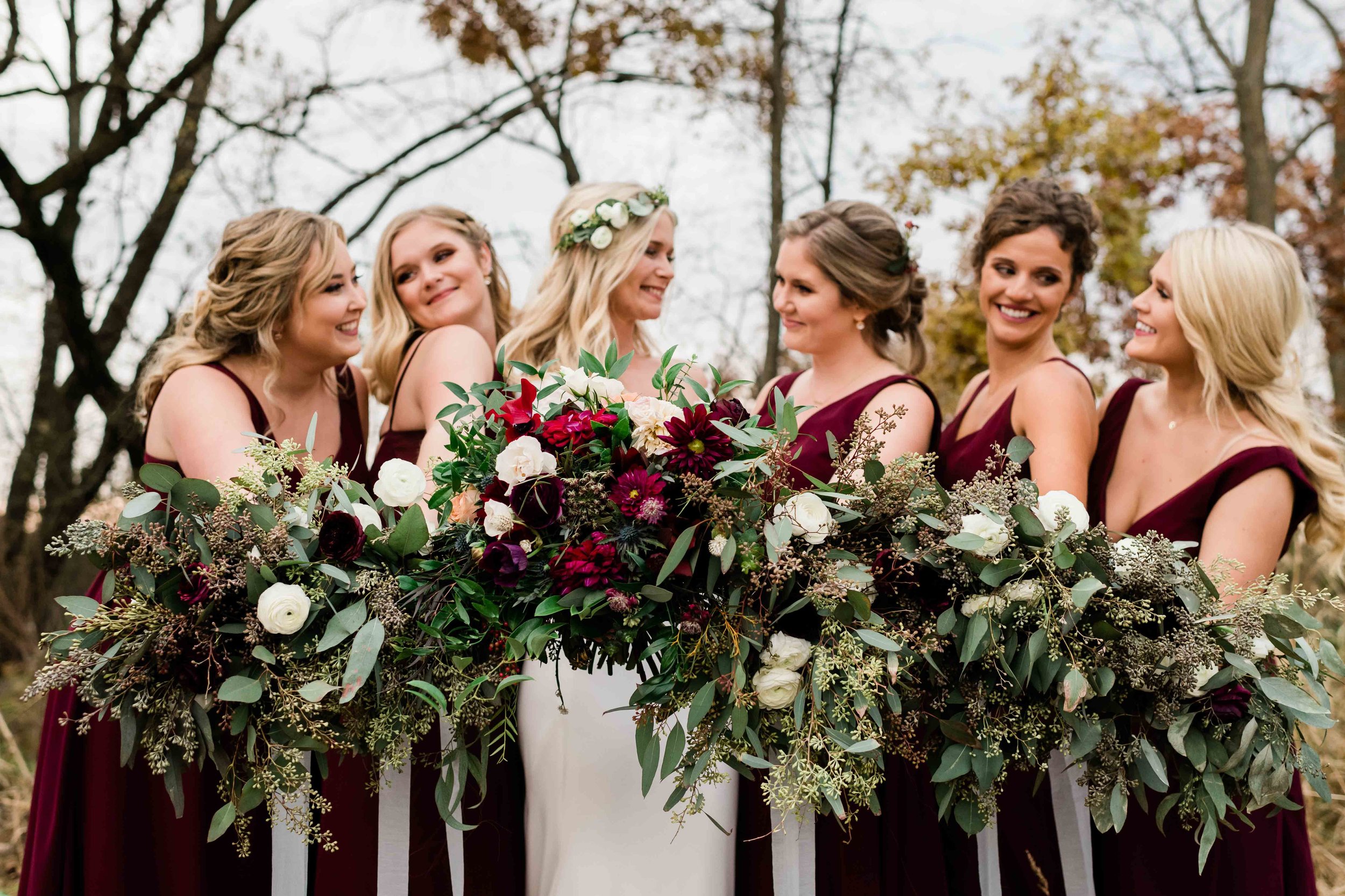 Bride and bridesmaids smile at each other as they hold out their bouquets