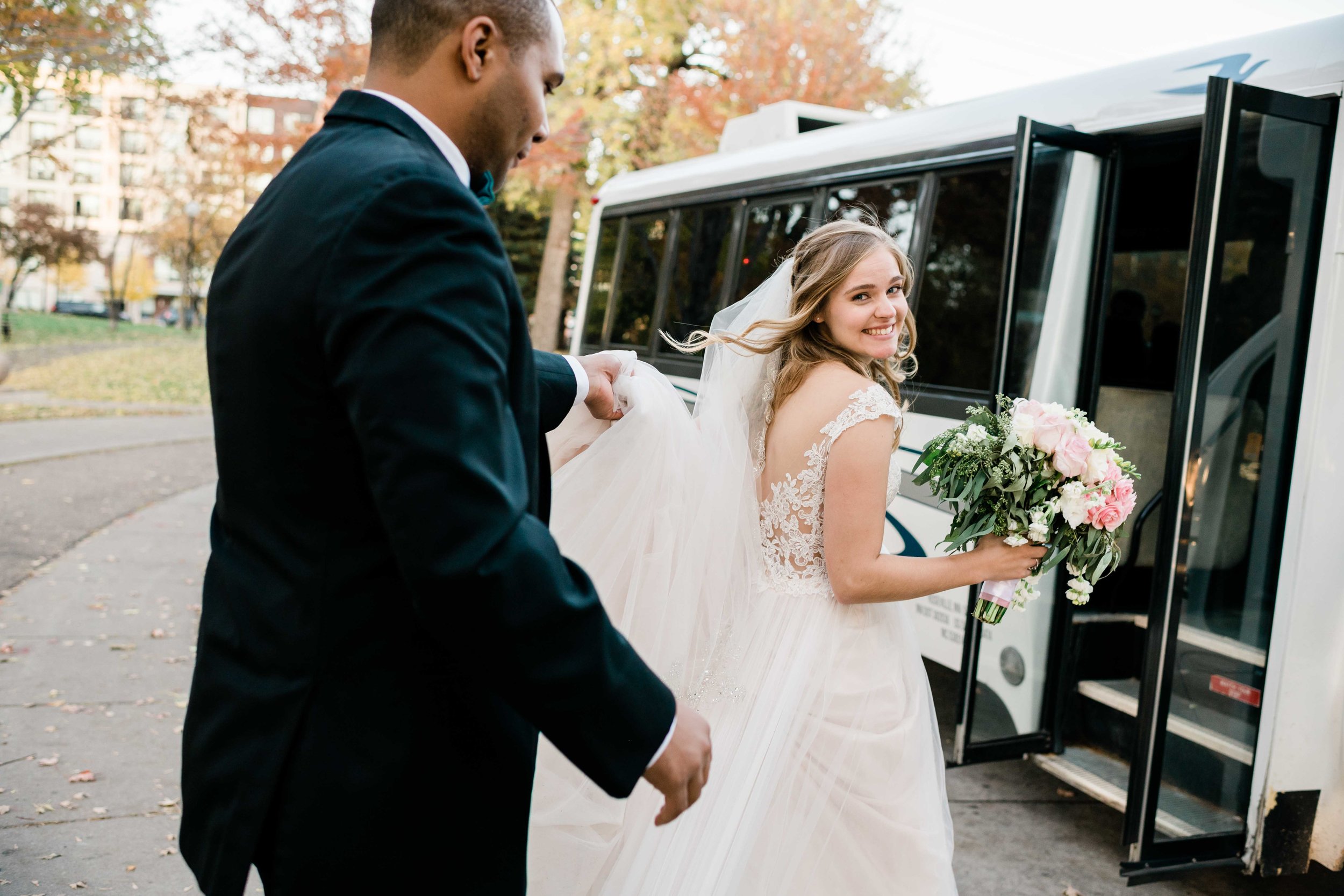 Groom holding up bride's veil as they approach shuttle bus