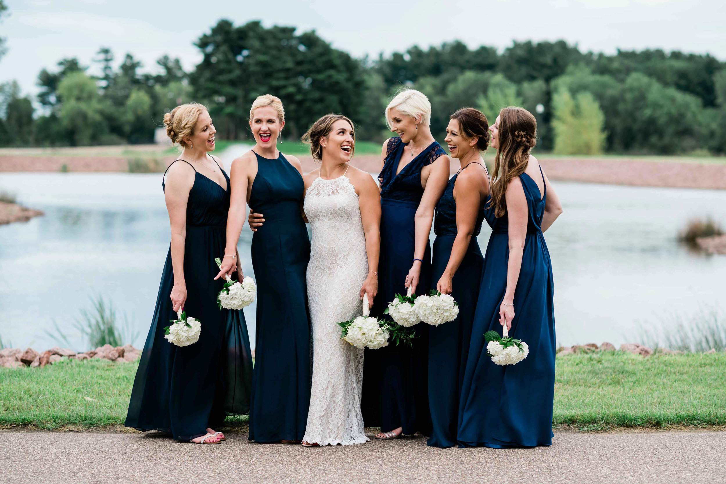 Bride and bridesmaids hold bouquets down as they laugh with each other