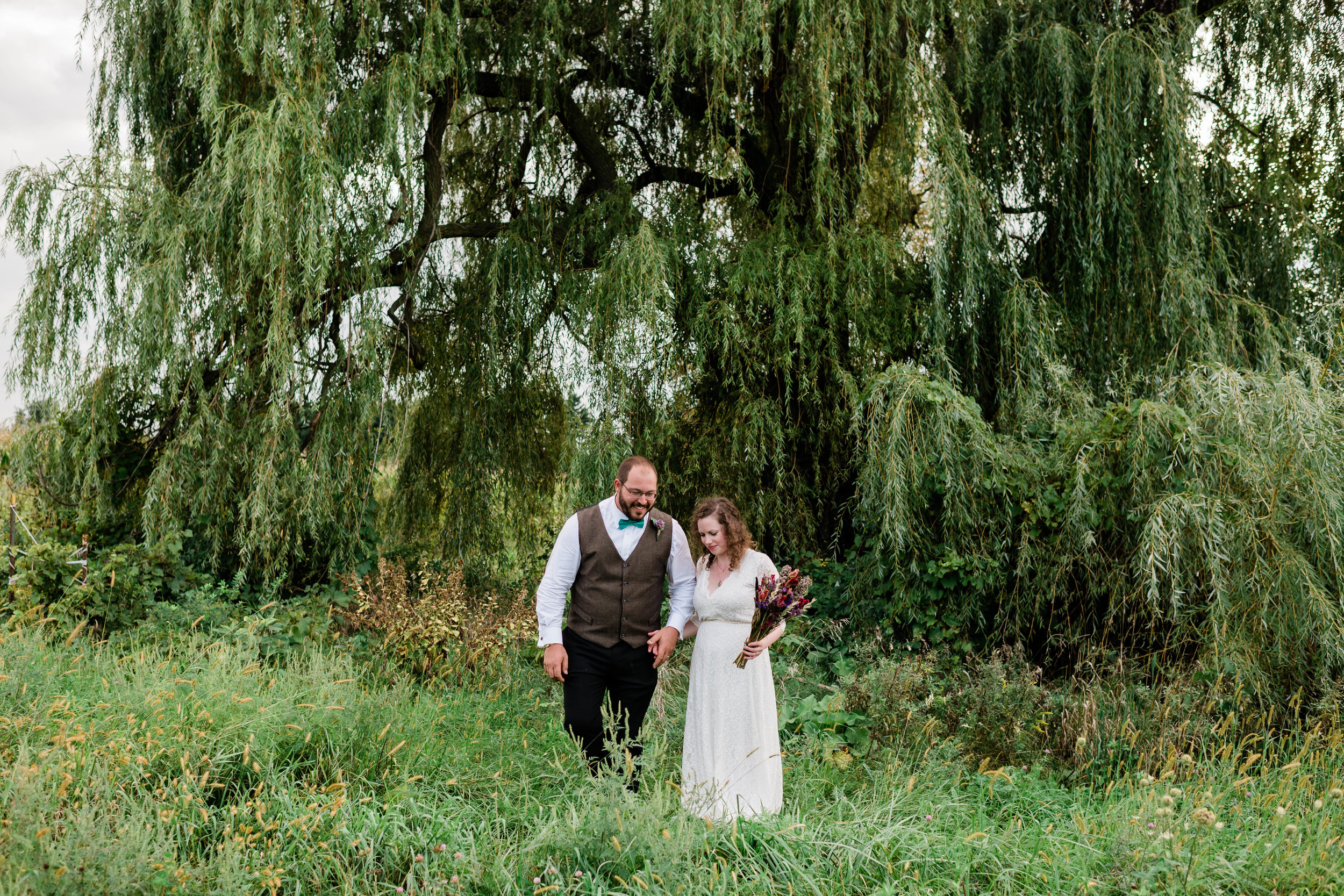 Bride and groom walk in front of a weeping willow tree