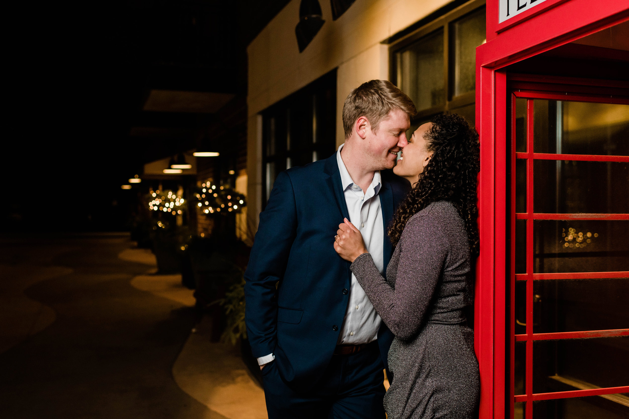 Engaged couple lean against red telephone booth