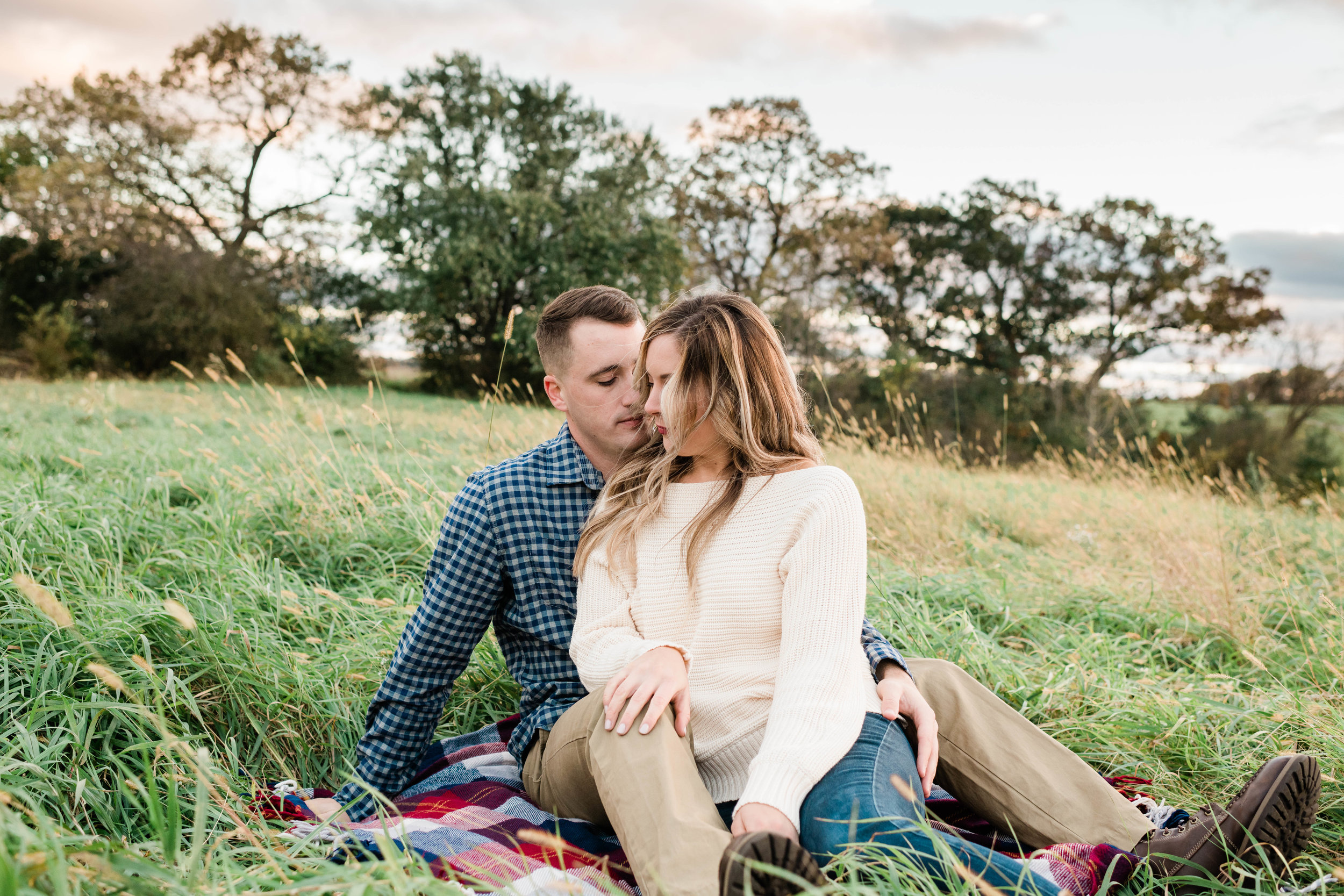 Engaged couple sits on a picnic blanket