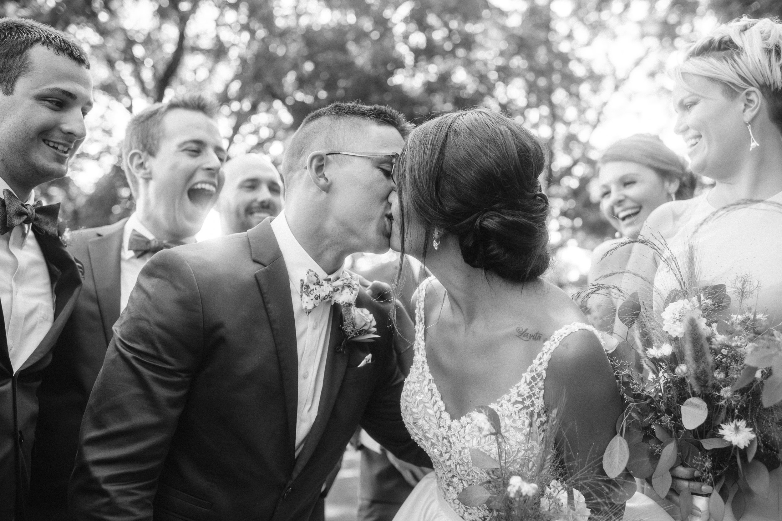 Bride and groom kissing while wedding party cheers