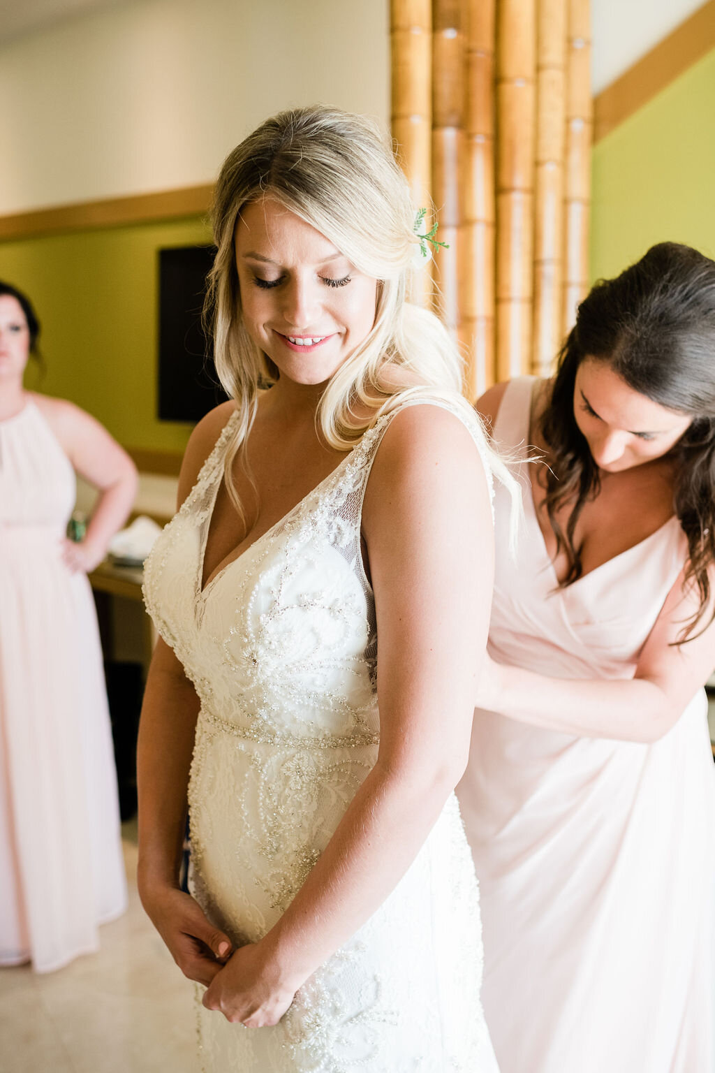 Bridesmaid buttoning up bride's wedding dress