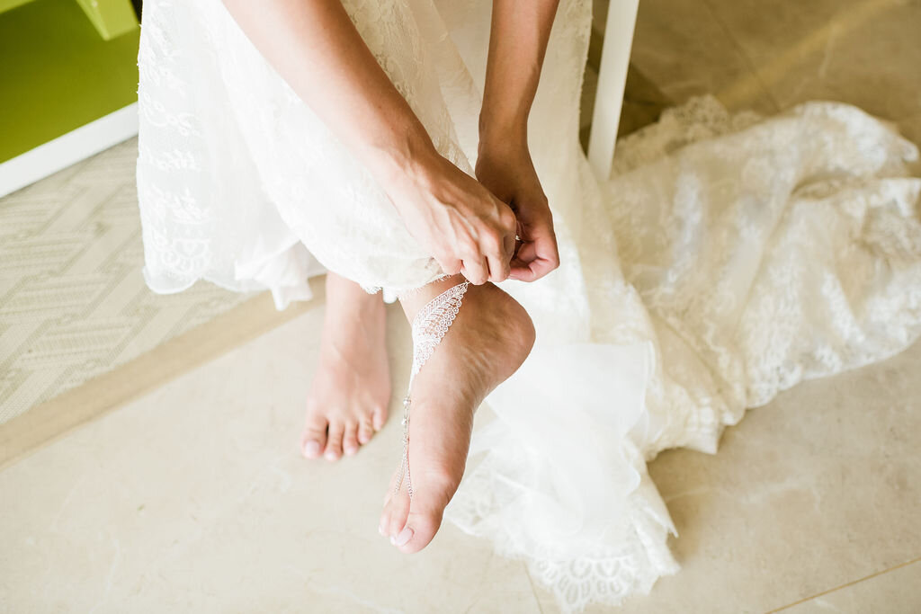 Bride putting on beaded barefoot beach sandals