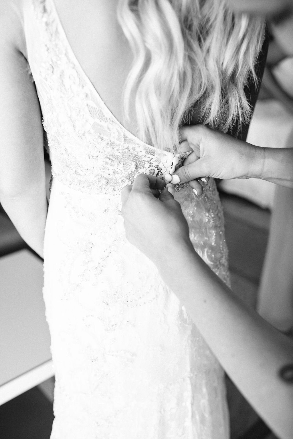 Closeup of bridesmaid buttoning up bride's wedding dress
