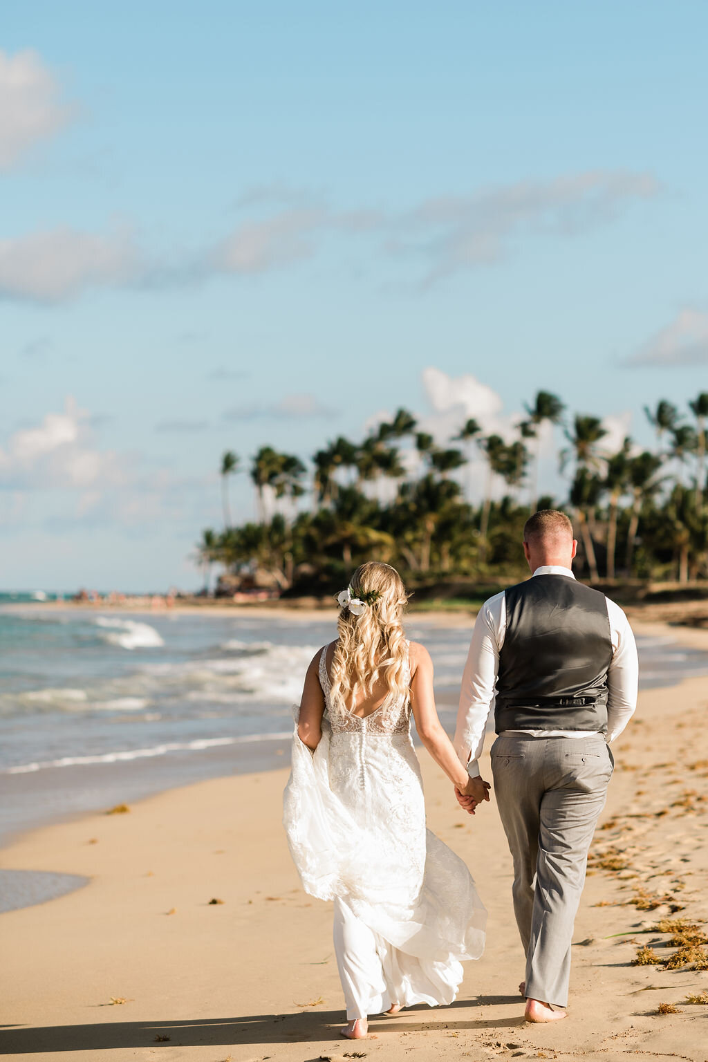 Bride and groom holding hands and walking away on the beach