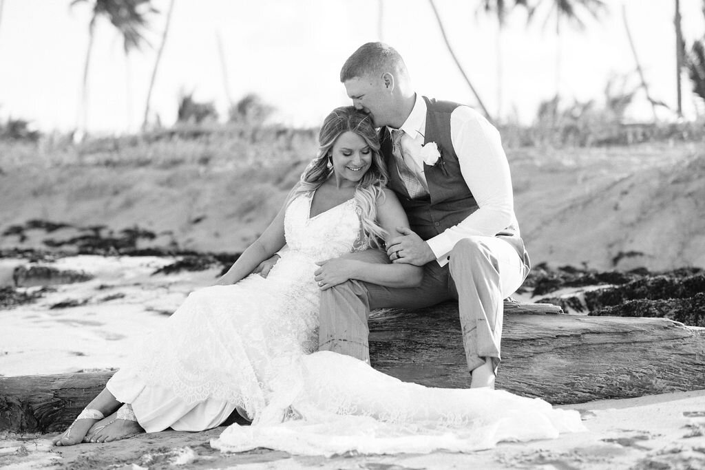 Bride and groom sitting on driftwood on the beach