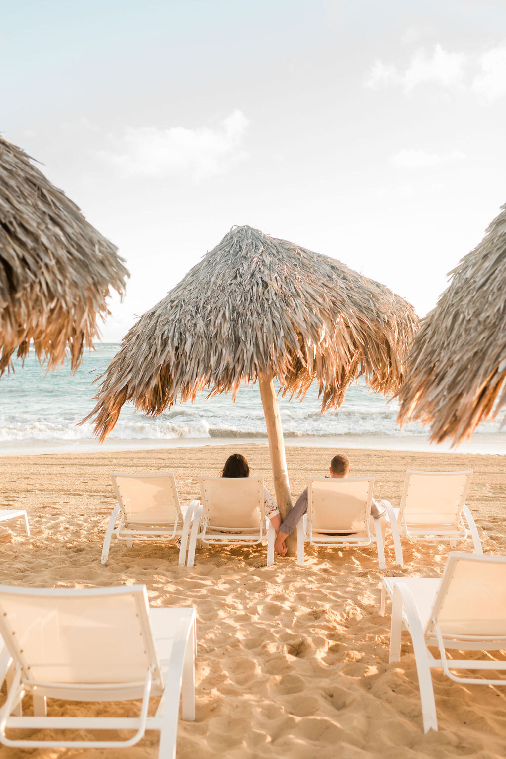 Engaged couple holding hands while sitting in chairs on the beach