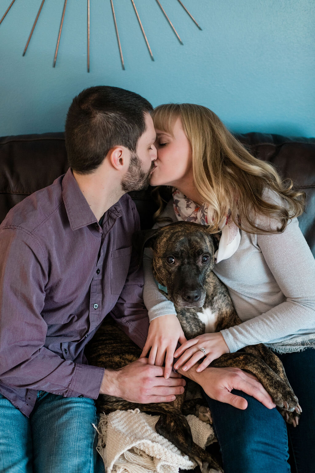 Engaged couple kissing on the couch with their dog