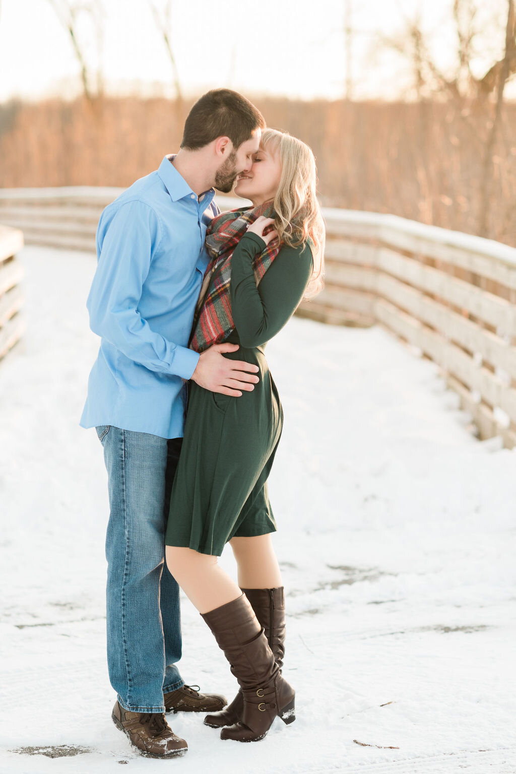 Engaged couple kissing on a snowy bridge
