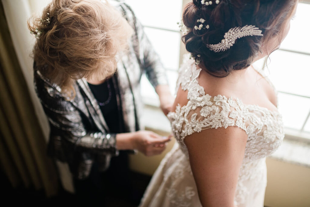 Mother of the bride buttoning up bride's wedding dress