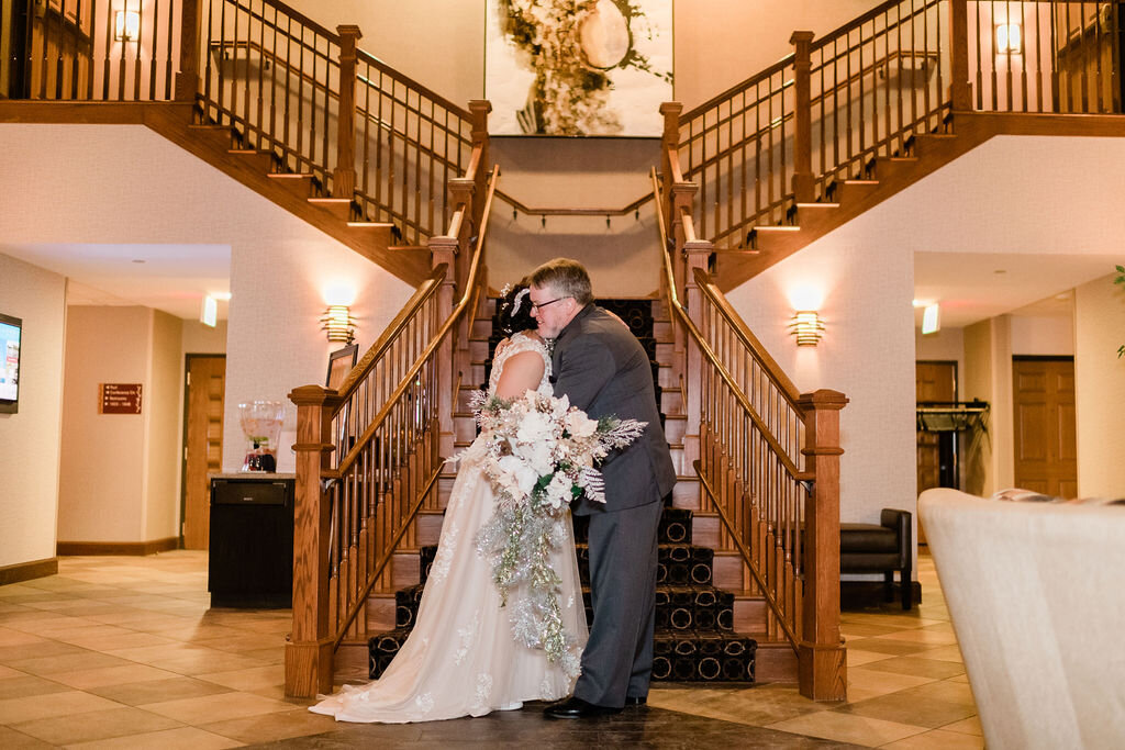 Bride and father hugging in front of the hotel staircase