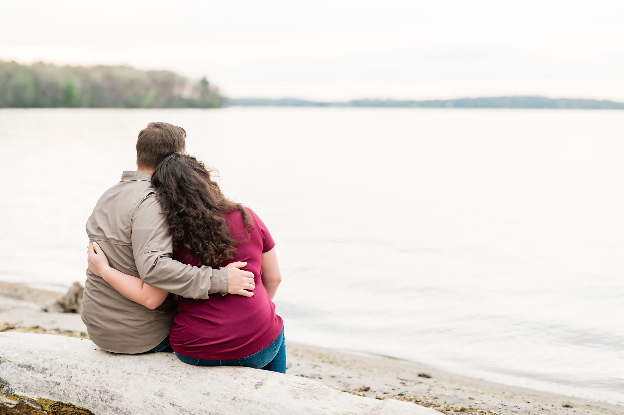 Engaged couple sitting on a log and look at the lake