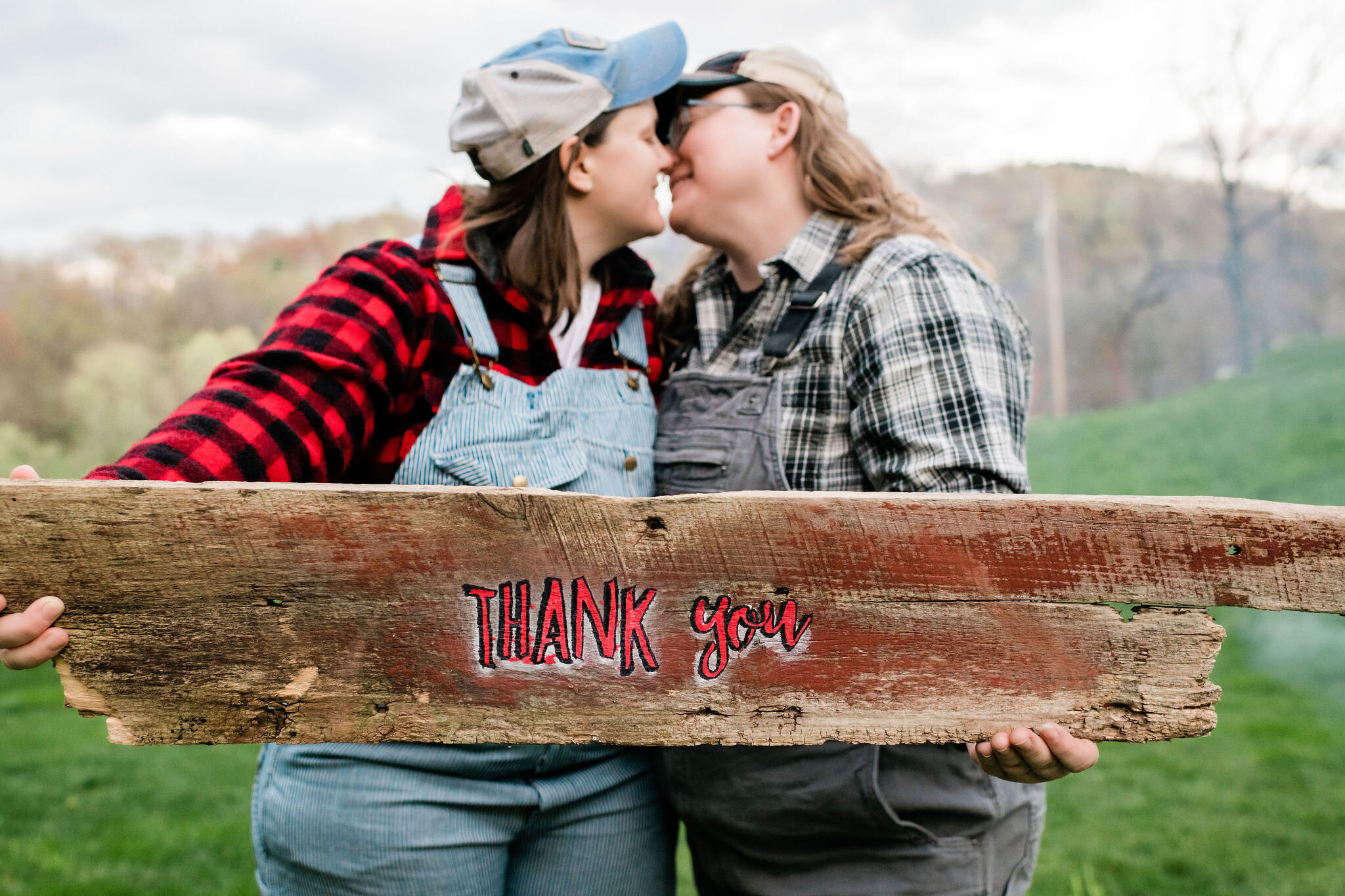 Women kissing behind a thank you sign they are holding