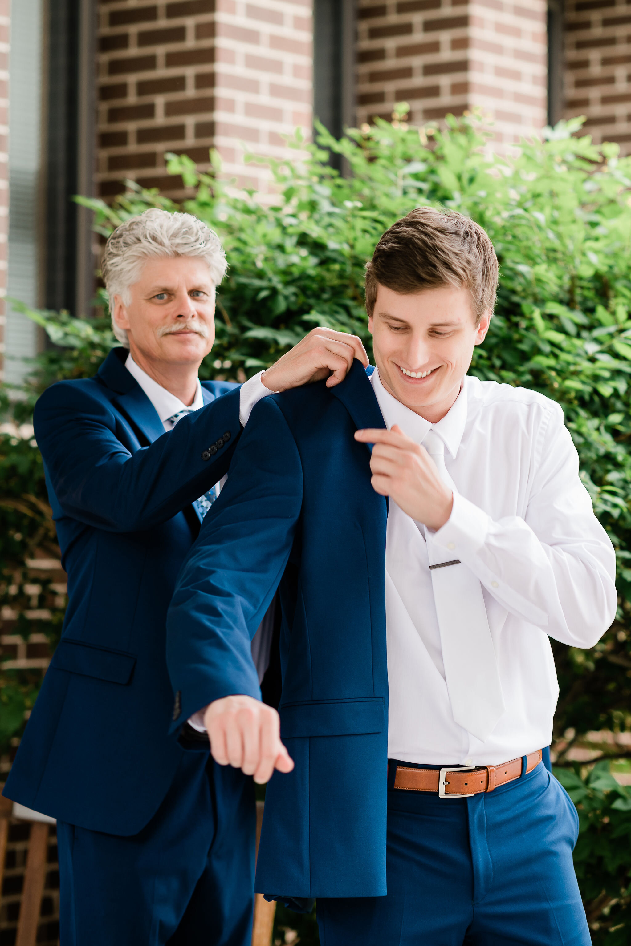 Groom's father putting on the groom's suit jacket 