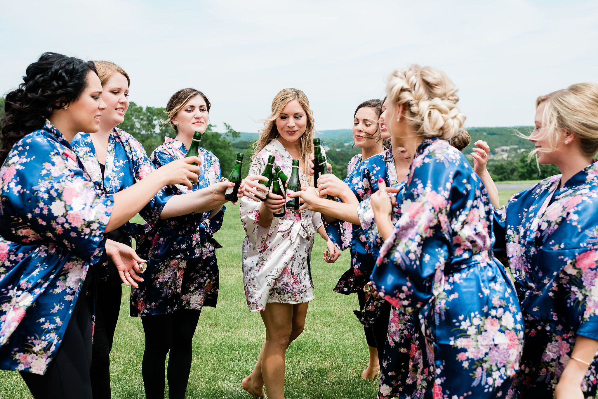 Bride and bridesmaids clinking personal champagne bottles together