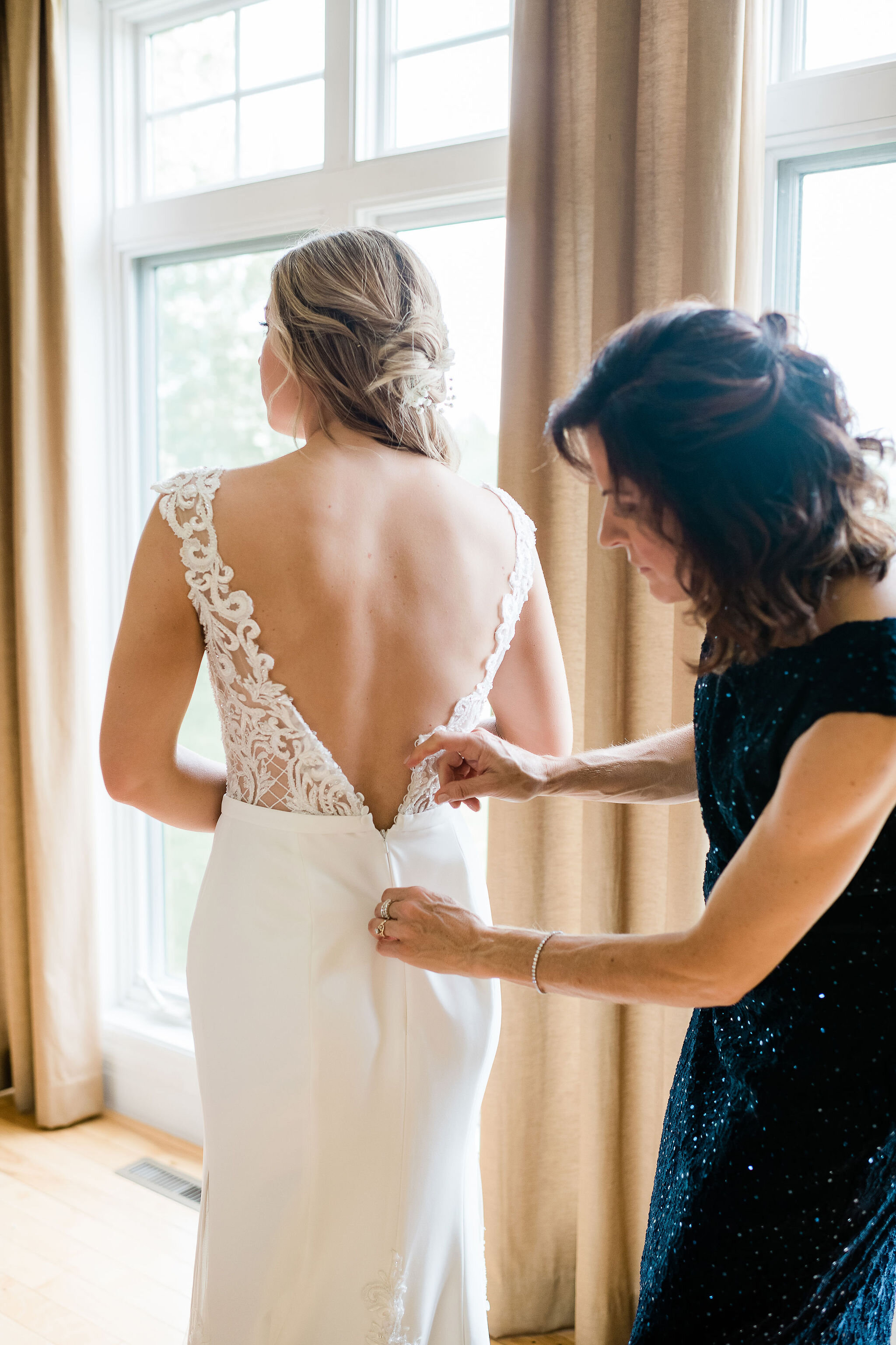 Mother of the bride zipping up bride's wedding dress