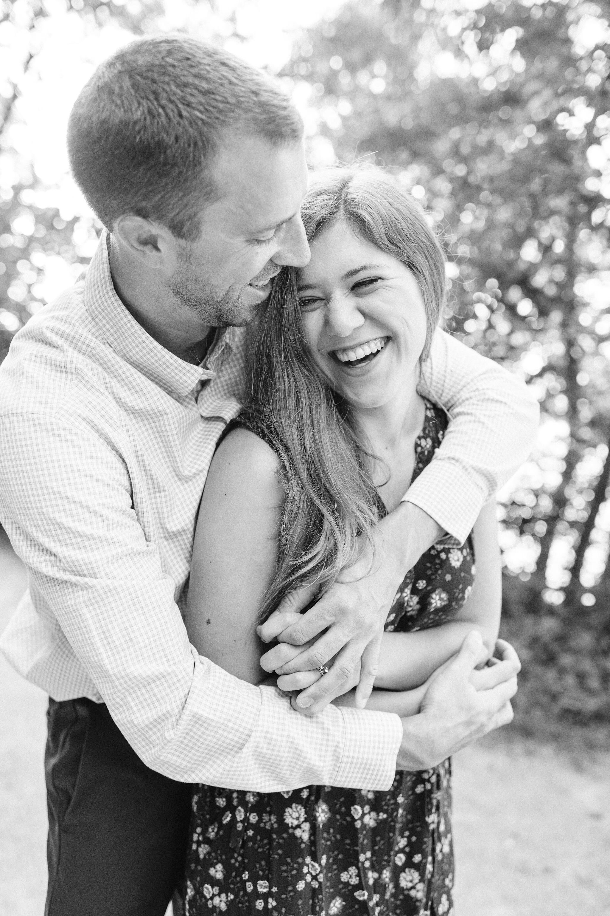 Woman laughs while her fiancé's arms are wrapped around her