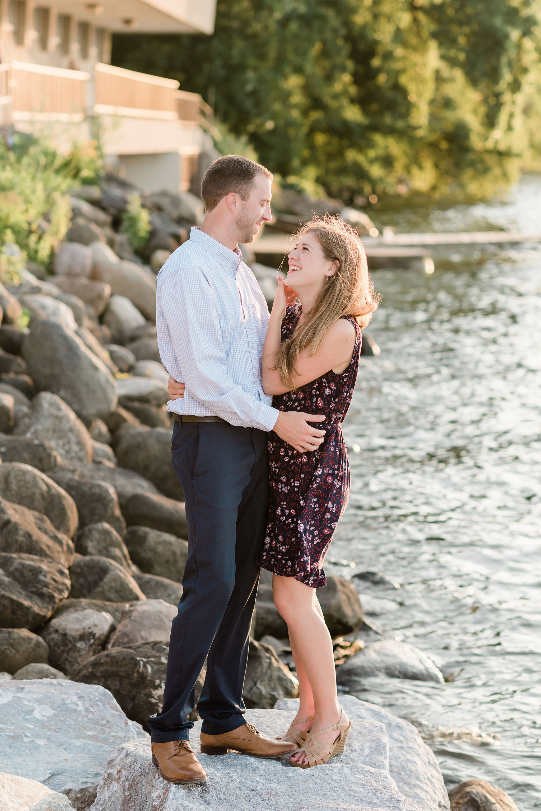 Engaged couple standing on rocks by the water