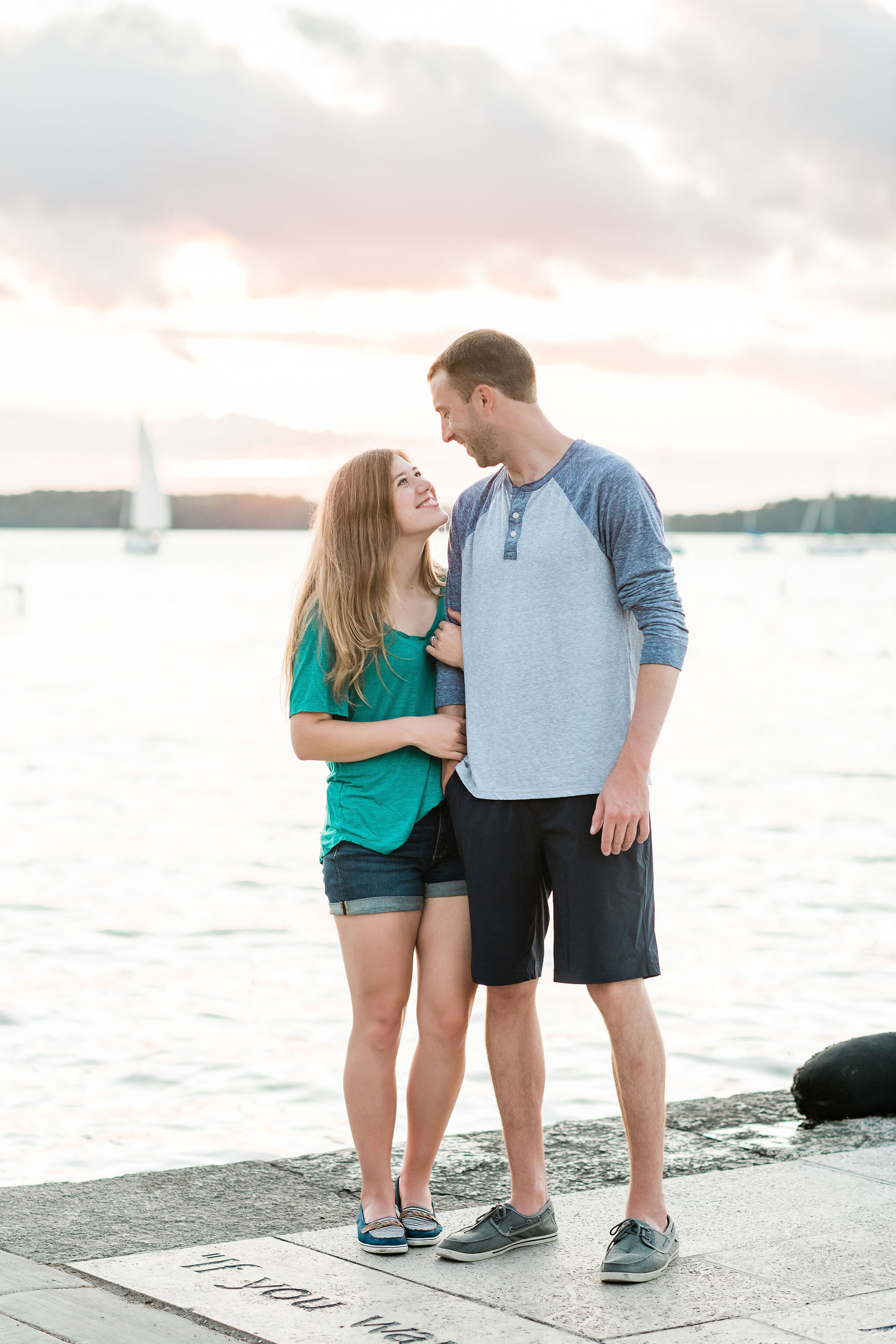 Engaged couple on a dock with a sailboat in the background