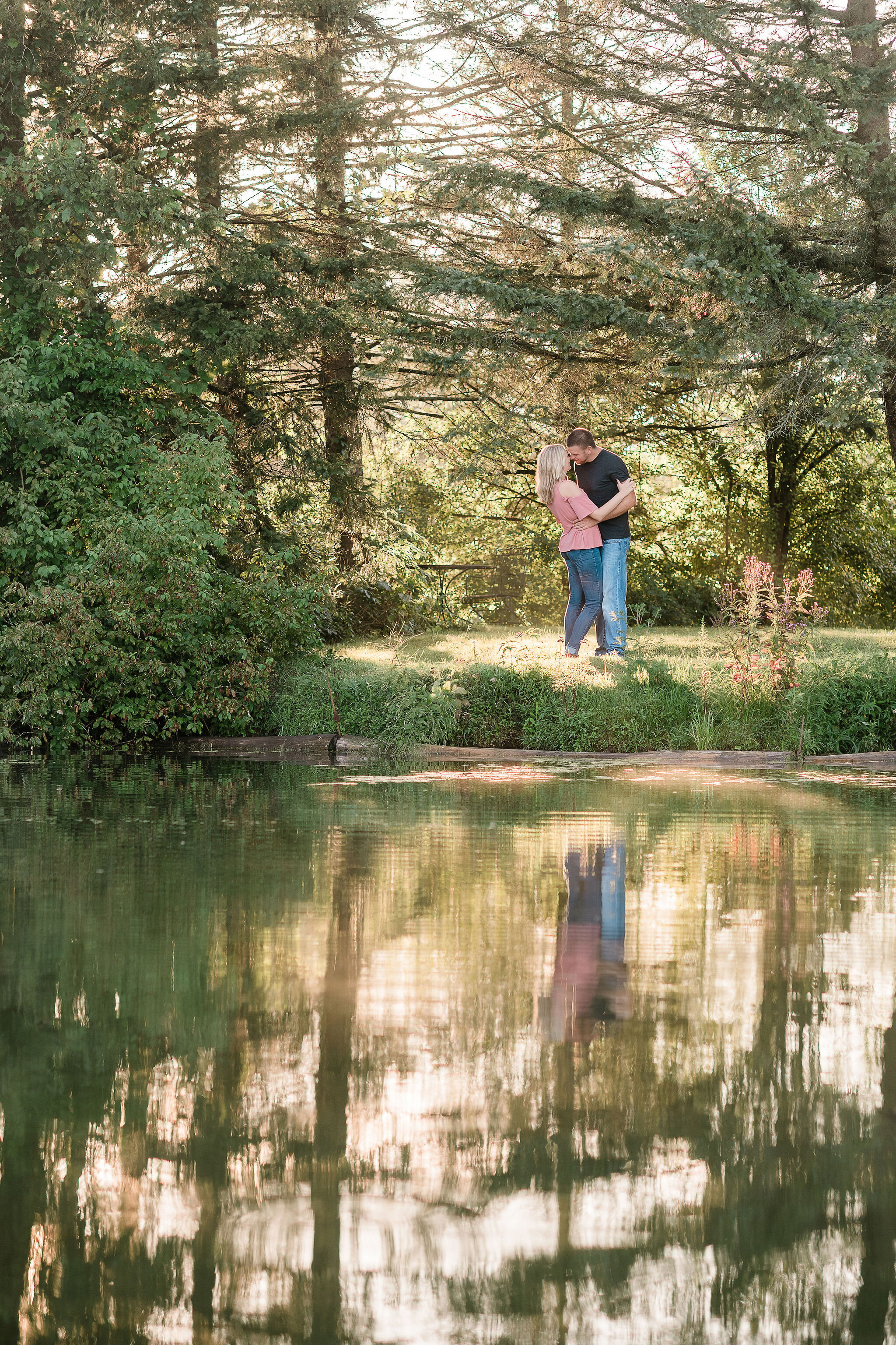 Engaged couple kissing by some trees and a pond