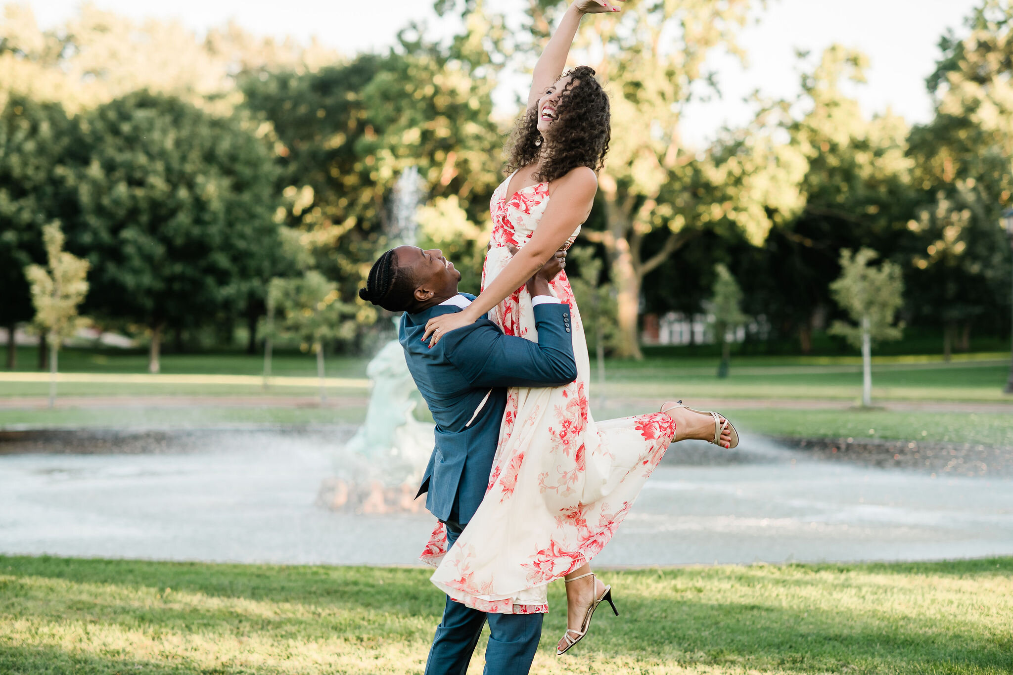 Woman raising her hand in the air as her fiancé picks her up