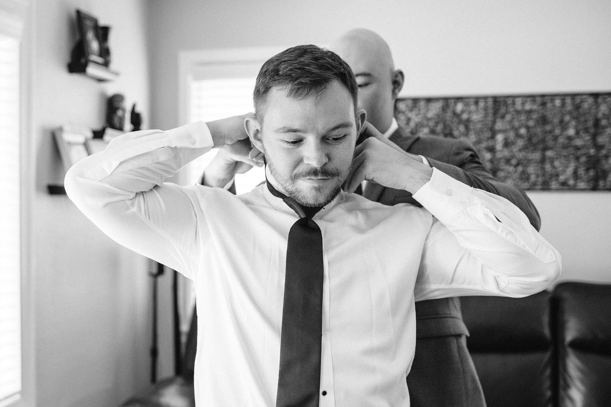 Groomsman helps groom put his tie on