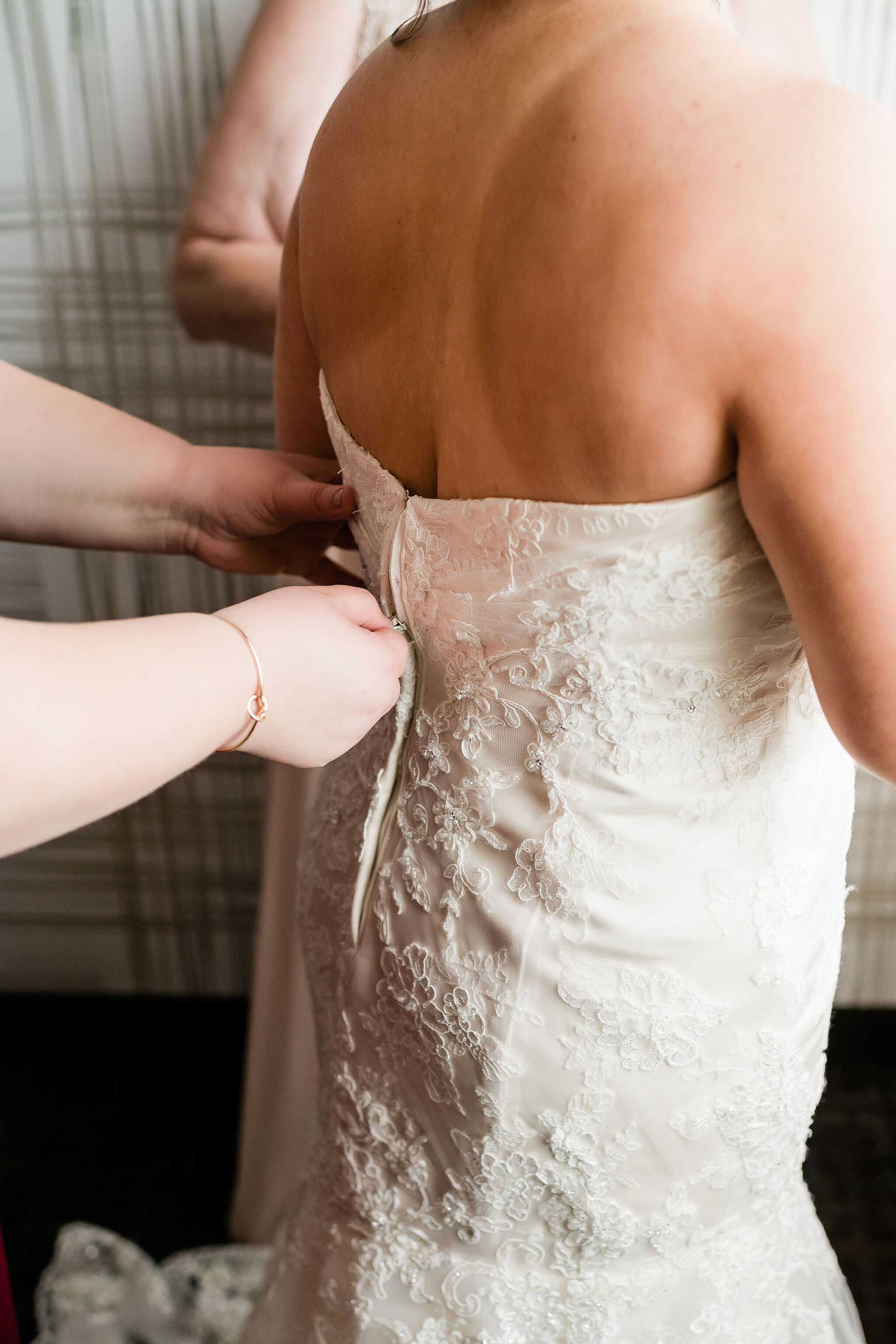 Bridesmaid zipping up bride's wedding dress