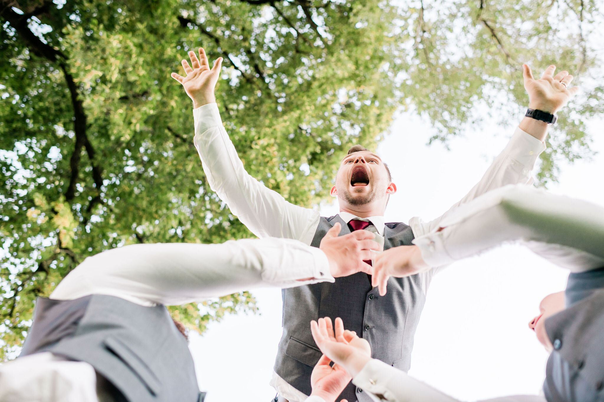 Groom being thrown up in the air by the groomsmen