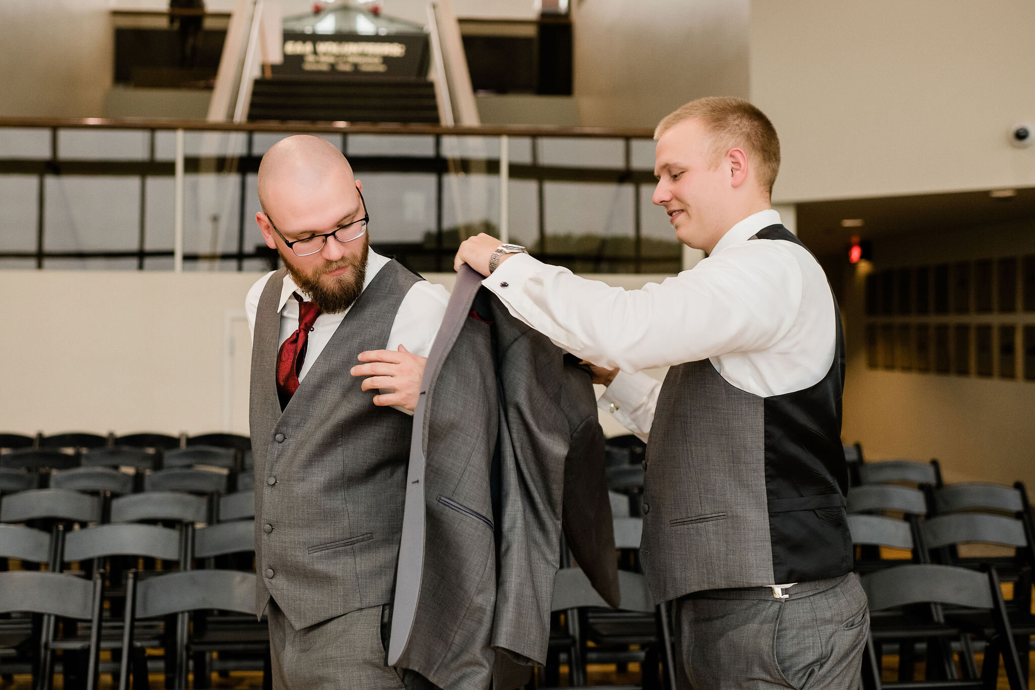 Groomsman helping groom into his suit jacket