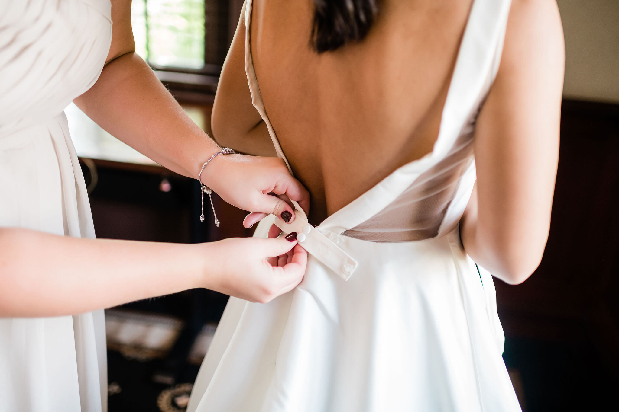 Bridesmaid buttoning up bride's dress