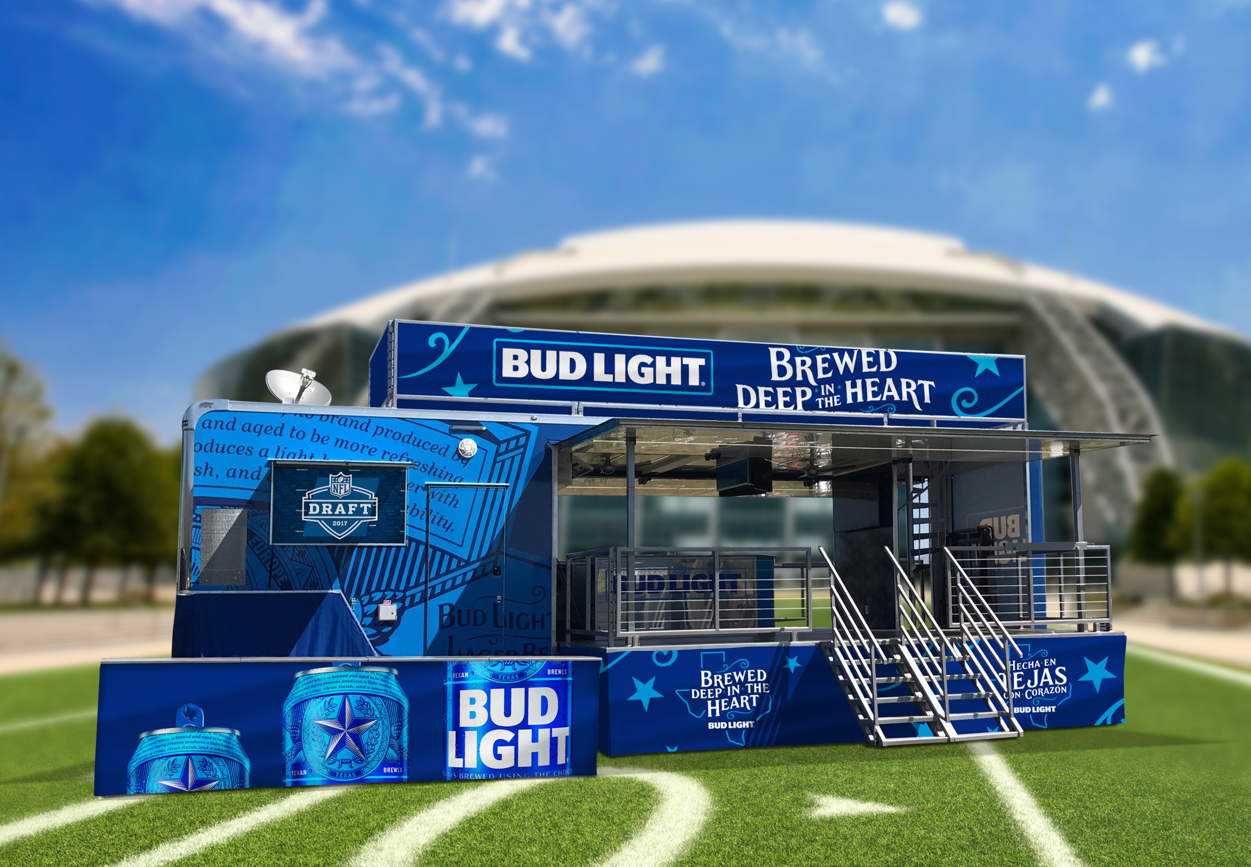 A blue promotional booth for Bud Light featuring the slogan "Brewed Deep in the Heart" with cans and signs, set up on a green football field with a stadium in the background.