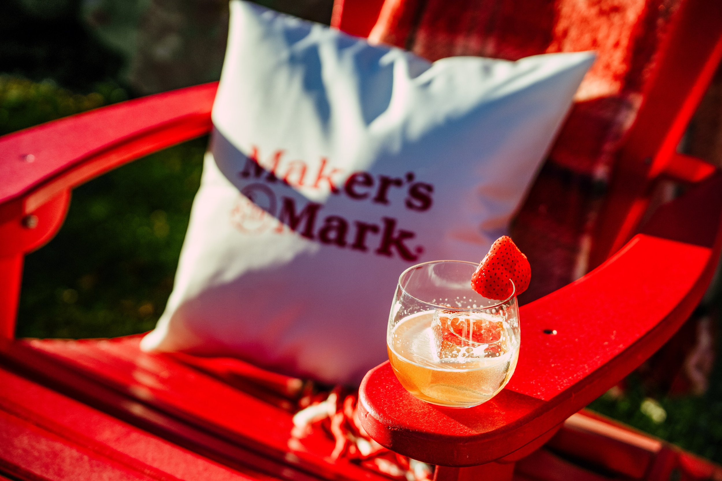 A glass of champagne garnished with a strawberry on a red table with a red bag and a white paper bag labeled "Mother's Market" in the background.