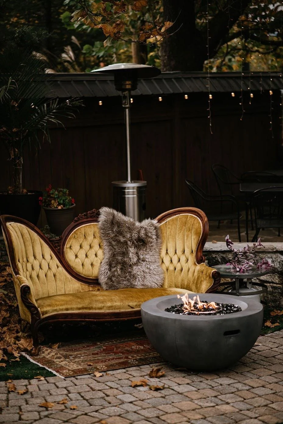 An antique couch with gold colored felt fabric with a fur blanking on top sitting in front of a fire pit at an Asheville wedding venue.